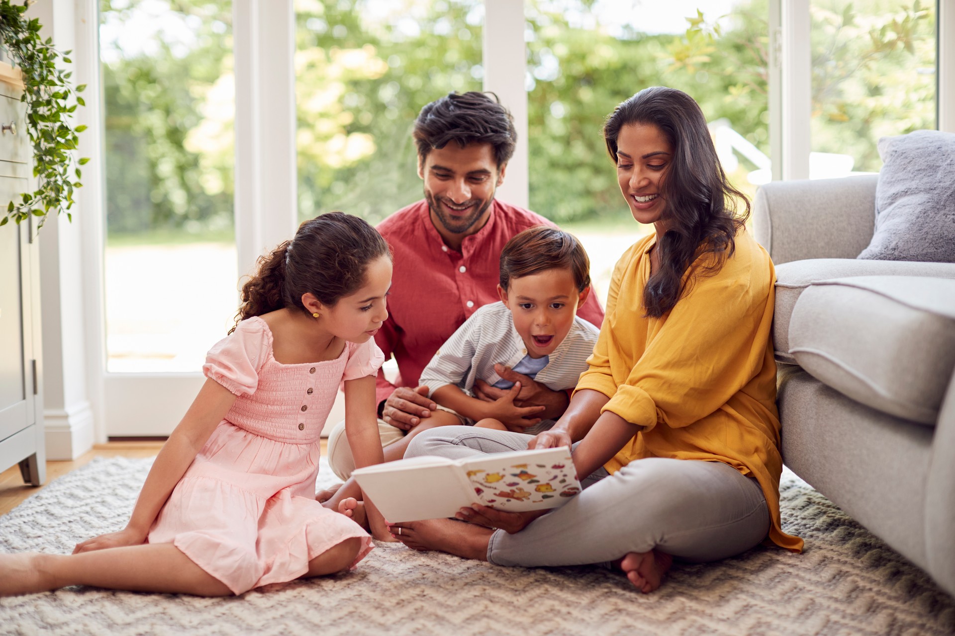 Family At Home Sitting On Floor In Lounge Reading Book Together